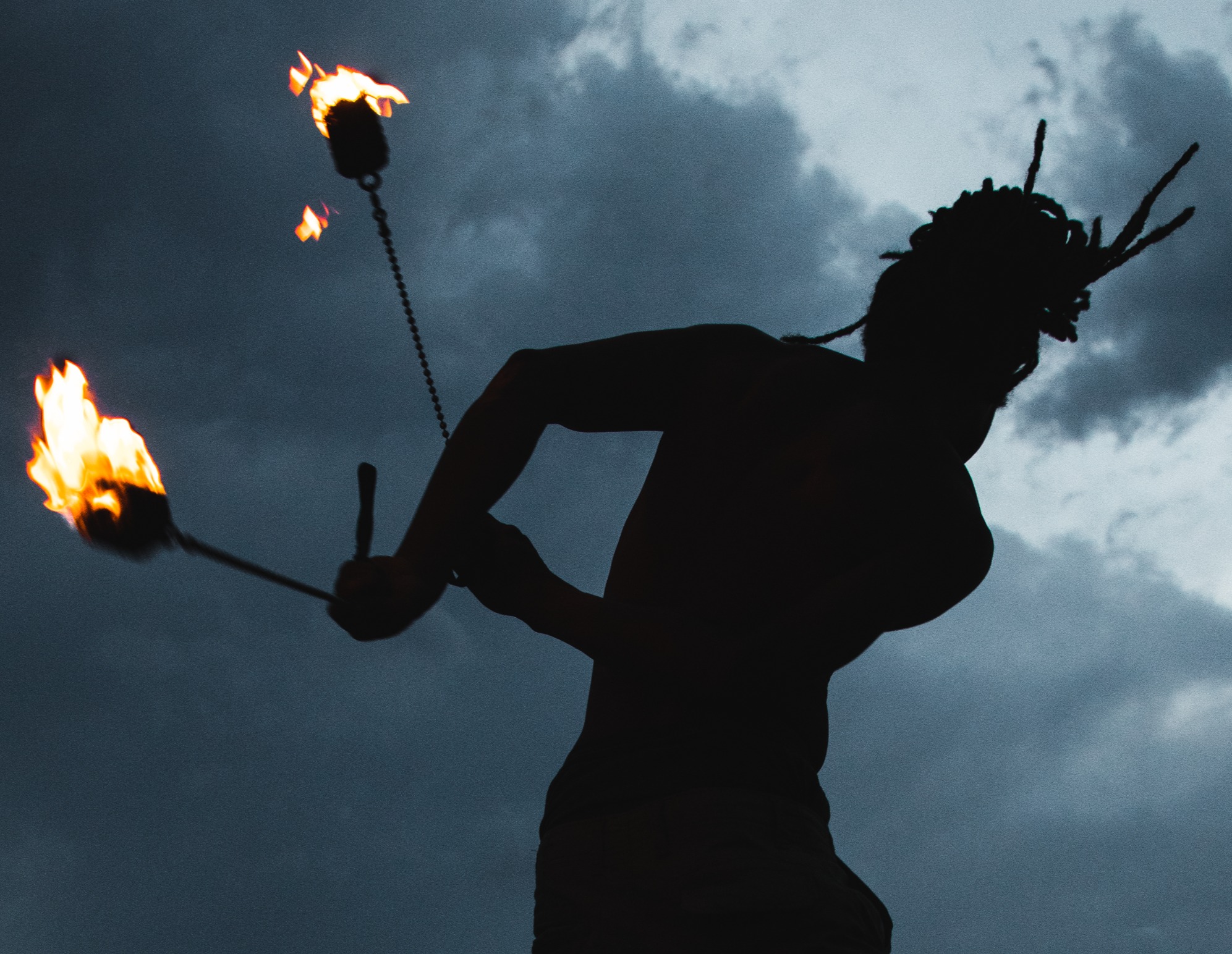 Nick May silhouette with fire poi against dramatic sky